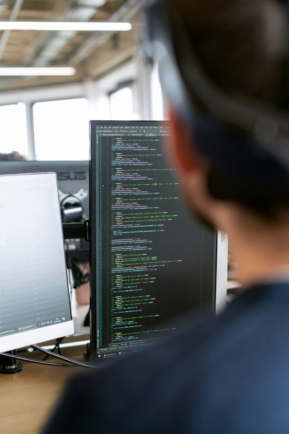 A person writing code on a monitor, seen from behind